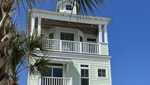 A multi-story building with a balcony on the second floor, a small tower-like structure on the roof, and a white fence in the foreground. - Poolside House w/ Ocean Views, Steps from Beach & Restaurants (Atlantic Beach)
