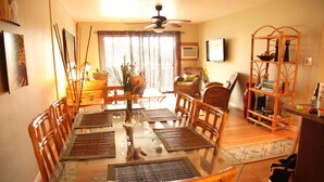 A dining area with a glass table, wicker chairs, and a ceiling fan. - Shores of Maui - Ocean View- Top Floor Unit--Spacious! AC & WiFi (Kihei)