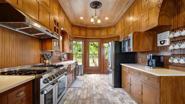 A kitchen with wooden cabinets, a stove, oven, refrigerator, and a coffee maker. - Charming Victorian Home w/Pickle Ball Court, Pool, Hot Tub, Game Room (San Marcos)