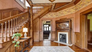 A grand staircase with ornate woodwork and a chandelier, leading to a room with a fireplace and a large mirror. - Charming Victorian Home w/Pickle Ball Court, Pool, Hot Tub, Game Room (San Marcos)
