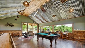 A spacious indoor area with a pool table, wooden furniture, and large windows offering views of the outdoors. - Charming Victorian Home w/Pickle Ball Court, Pool, Hot Tub, Game Room (San Marcos)