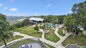 A modern house with a stone deck, a swimming pool, and a scenic view of the mountains. - Charming Victorian Home w/Pickle Ball Court, Pool, Hot Tub, Game Room (San Marcos)