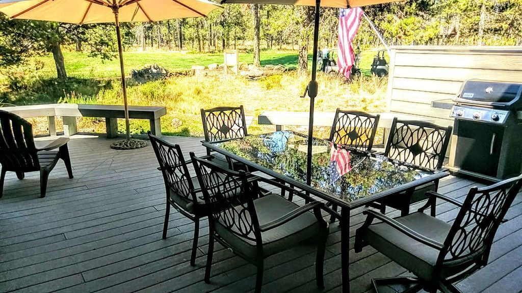 A deck with a glass-top table and chairs, surrounded by a grill and an American flag.