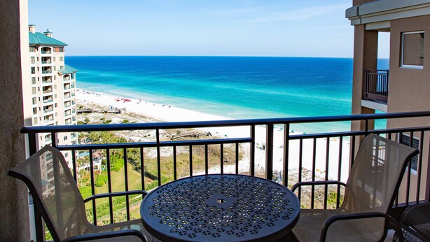 A balcony with a table and chairs overlooking a beach and ocean.