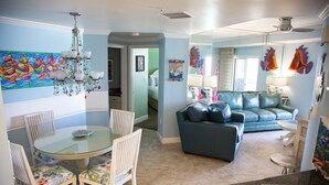 A dining area with a glass table and chairs, a blue sofa, and a chandelier.