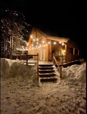 A log cabin with a staircase leading to the entrance, surrounded by snow.