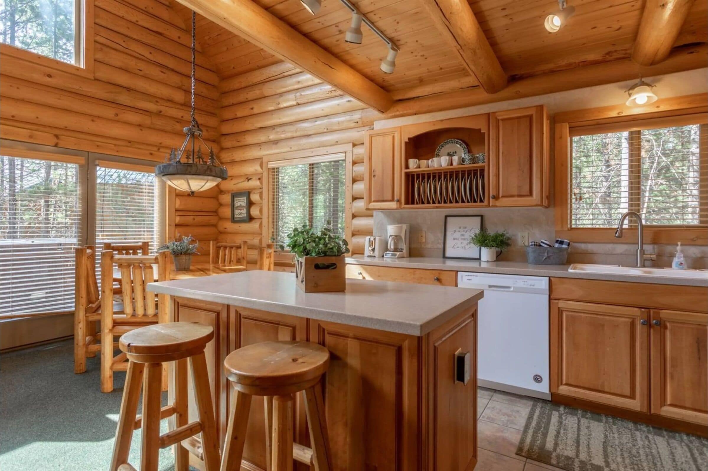 Interior de una cabaña de madera con zona de cocina, taburetes de bar y mesa de comedor.