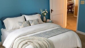 A bedroom with a bed, a nightstand, a vase with flowers, and a door leading to a dining area. - Lake House on Seneca Lake with Private Dock (Romulus)
