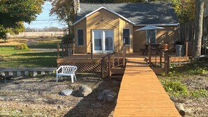 A wooden house with a deck leading to a small porch, surrounded by trees and a stream. - Lake House on Seneca Lake with Private Dock (Romulus)