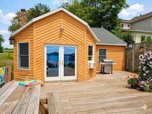 A wooden cabin with a deck, a sliding glass door, and a barbecue grill.