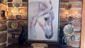 Un interior rústico con un cuadro de un caballo enmarcado, platos decorativos y un mueble de madera con cajones.