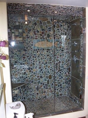 A shower with a mosaic tile design and a glass door.