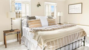 Een slaapkamer met een bed, twee nachtkastjes, een wandlamp en een ingelijste citaat aan de muur.