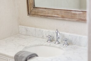 Un baño con encimera de mármol, un lavabo y dos grifos.