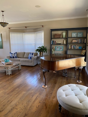 A living room with a grand piano, a sofa, a coffee table, and a bookshelf.