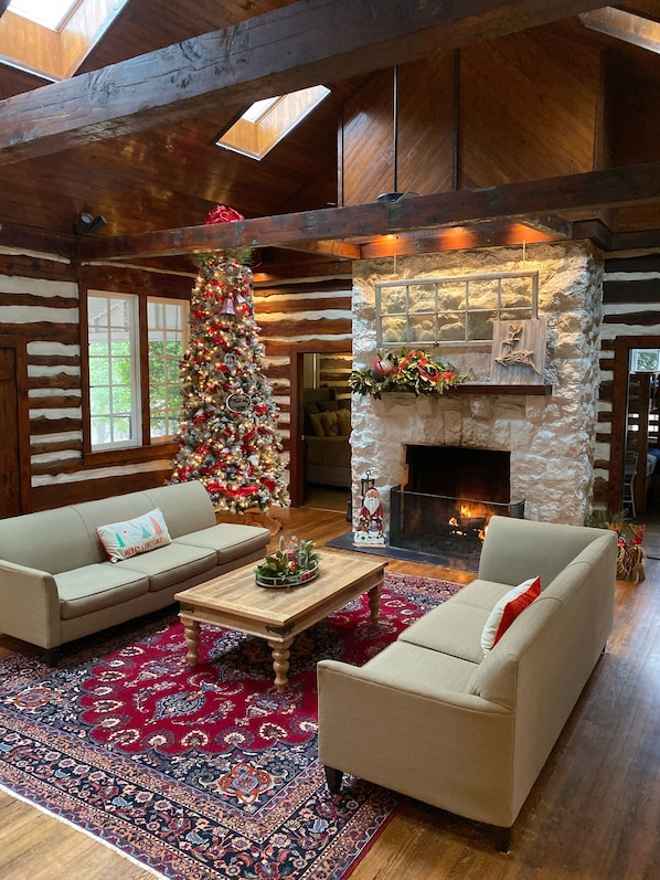 A log cabin interior with a Christmas tree, two sofas, a fireplace, and a stone wall.