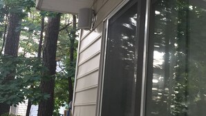 A house with a large sliding glass door, a white exterior, and a tree in the background.