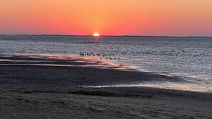 A sunset over a beach with waves and a distant horizon.