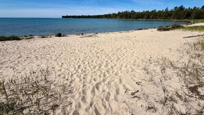 Ein Sandstrand mit Fußabdrücken, ein klarer Himmel und eine bewaldete Küstenlinie.