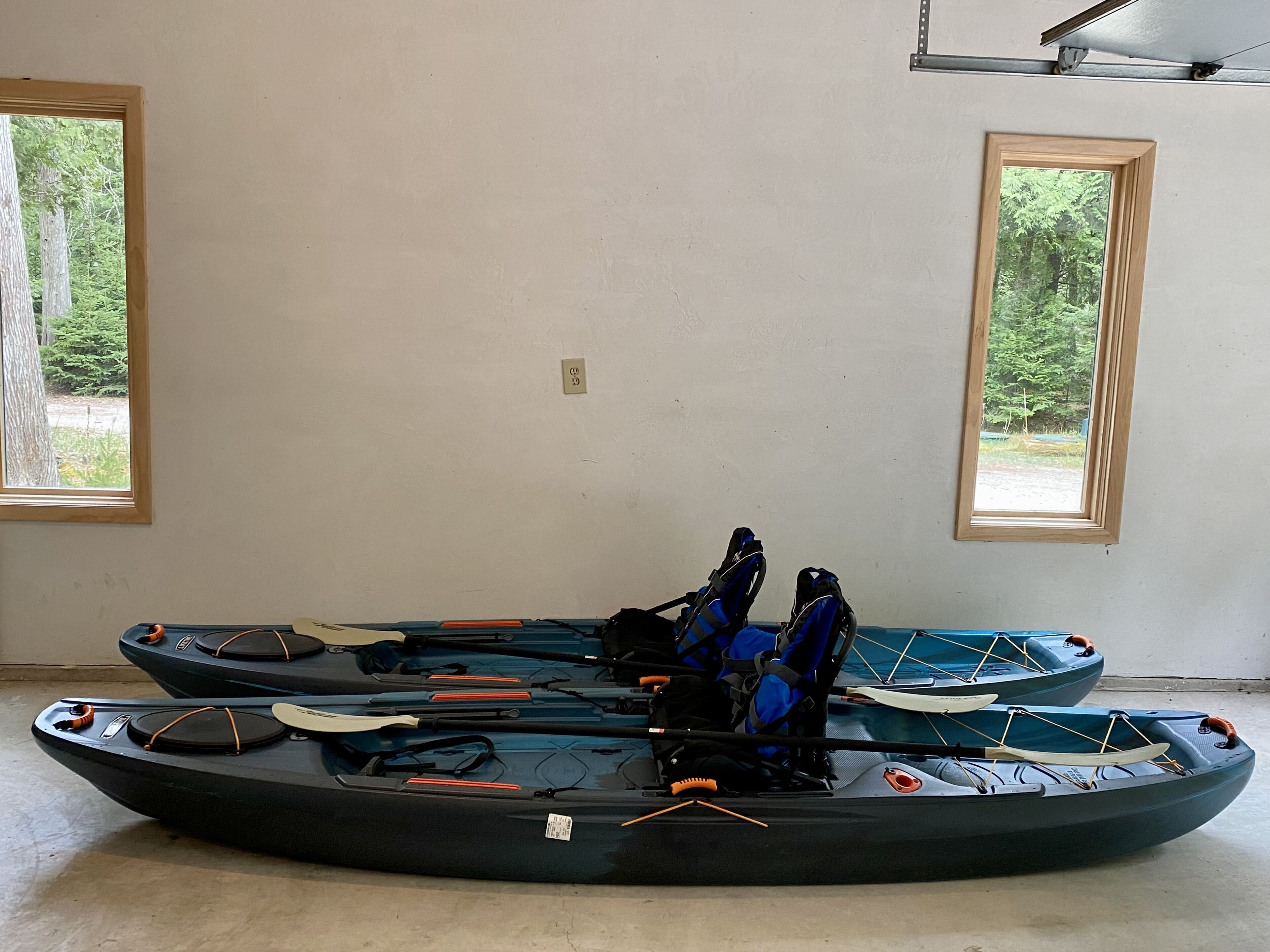Two kayaks in a room with large windows.