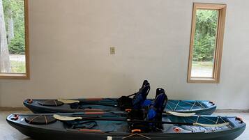 Two kayaks in a room with large windows.