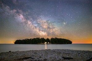 Ein sternenklarer Nachthimmel über einem stillen See mit einer bewaldeten Insel im Hintergrund.