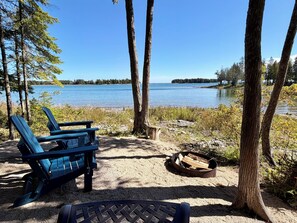 Un espace de camping au bord du lac, équipé de deux fauteuils Adirondack, d’un foyer et offrant une vue sur le lac et la rive éloignée.