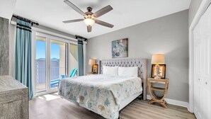 A bedroom with a bed, two bedside tables, a ceiling fan, and a view of a balcony.
