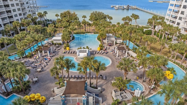 A resort with multiple swimming pools, palm trees, and a view of the ocean.