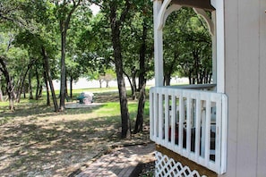 A covered outdoor area with a white railing, surrounded by trees and a brick pathway.
