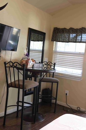 A small room with a desk, two chairs, a TV, a window with blinds, and a sign indicating a coffee bar.
