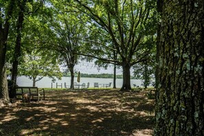 A park with a bench, tables, and chairs under trees by a lake. - Waterfront Hideaway Cabin | Private Lake Access & Stunning Views (Little Elm)