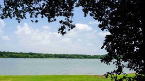 Un lac avec une étendue d’herbe au premier plan et des arbres qui encadrent la vue.