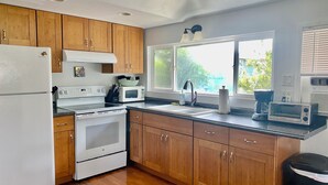 Una cocina con armarios de madera, un refrigerador blanco, una estufa, un microondas, un fregadero y una ventana con vista a la vegetación.