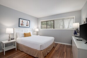A neatly arranged bedroom with a bed, bedside tables, a TV, and a window with blinds.