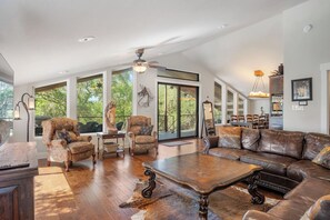A spacious living room with a large leather sofa, patterned armchairs, and a wooden coffee table.