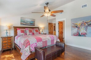 Ein Schlafzimmer mit einem hölzernen Bett, einer Sitzbank, einem Deckenventilator und einem Kuhbild.