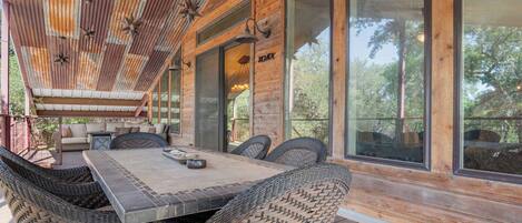 Une terrasse en bois avec une table à manger et des chaises en osier, de grandes fenêtres et un luminaire en forme d’étoile.