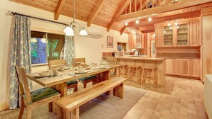 A spacious kitchen with wooden cabinets, a dining area with a long table and benches, and a high ceiling with exposed beams. - Cozy, clean, updated cabin w/hot tub, fireplace, fire pit, BBQ, smart TV (Packwood)