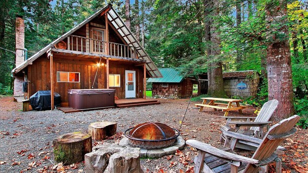 A rustic cabin with a hot tub, a fire pit, and a picnic table in a forest setting. - Cozy, clean, updated cabin w/hot tub, fireplace, fire pit, BBQ, smart TV (Packwood)
