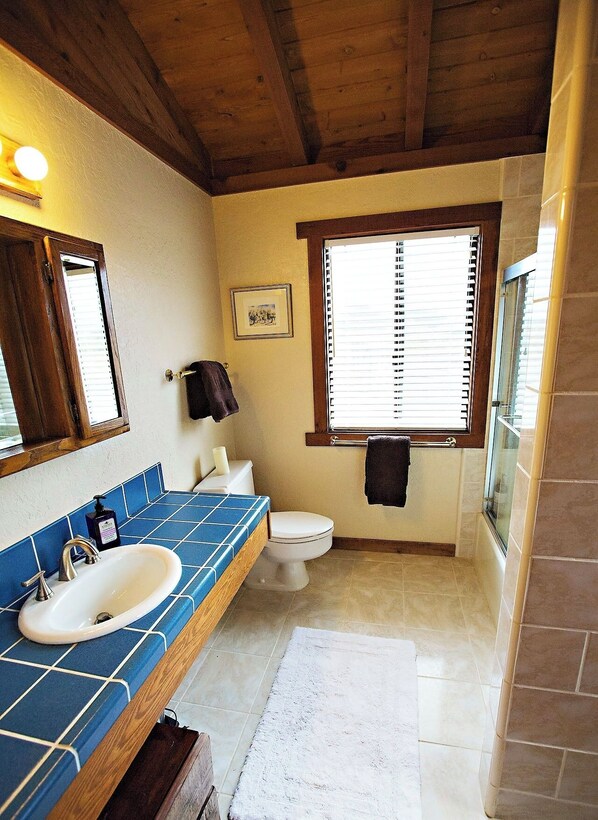 A bathroom with a wooden ceiling, a blue-tiled sink, a white toilet, and a window with blinds. - Ocean views. Long stay discount. Short walk to Shell beach, dog friendly. (Sea Ranch)
