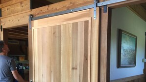A wooden sliding door in a room with a beige sofa and a painting on the wall. - Ocean views. Long stay discount. Short walk to Shell beach, dog friendly. (Sea Ranch)