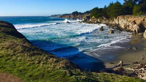 A coastal landscape with rocky cliffs, waves crashing onto the shore, and a clear blue sky. - Ocean views. Long stay discount. Short walk to Shell beach, dog friendly. (Sea Ranch)