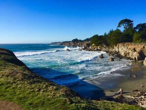 A coastal landscape with rocky cliffs, waves crashing onto the shore, and a clear blue sky. - Ocean views. Long stay discount. Short walk to Shell beach, dog friendly. (Sea Ranch)