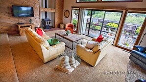 A spacious living room with two sofas, a coffee table, and a television. There is a large window providing a view of the outdoors. - Ocean views. Long stay discount. Short walk to Shell beach, dog friendly. (Sea Ranch)