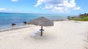 Une plage avec un parasol en chaume et des chaises longues blanches.