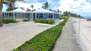 Un hôtel situé en bord de mer, doté d’un espace extérieur couvert avec des sièges, d’un chemin bordé de sable et de palmiers.