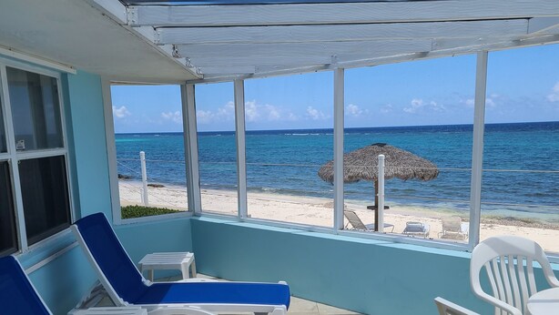 Un espace extérieur aménagé, abrité et doté de chaises longues bleues et blanches, d’une table et d’une vue sur la plage et l’océan.