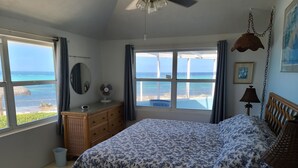 Une chambre à coucher avec un lit, une commode et de grandes fenêtres donnant sur la mer.