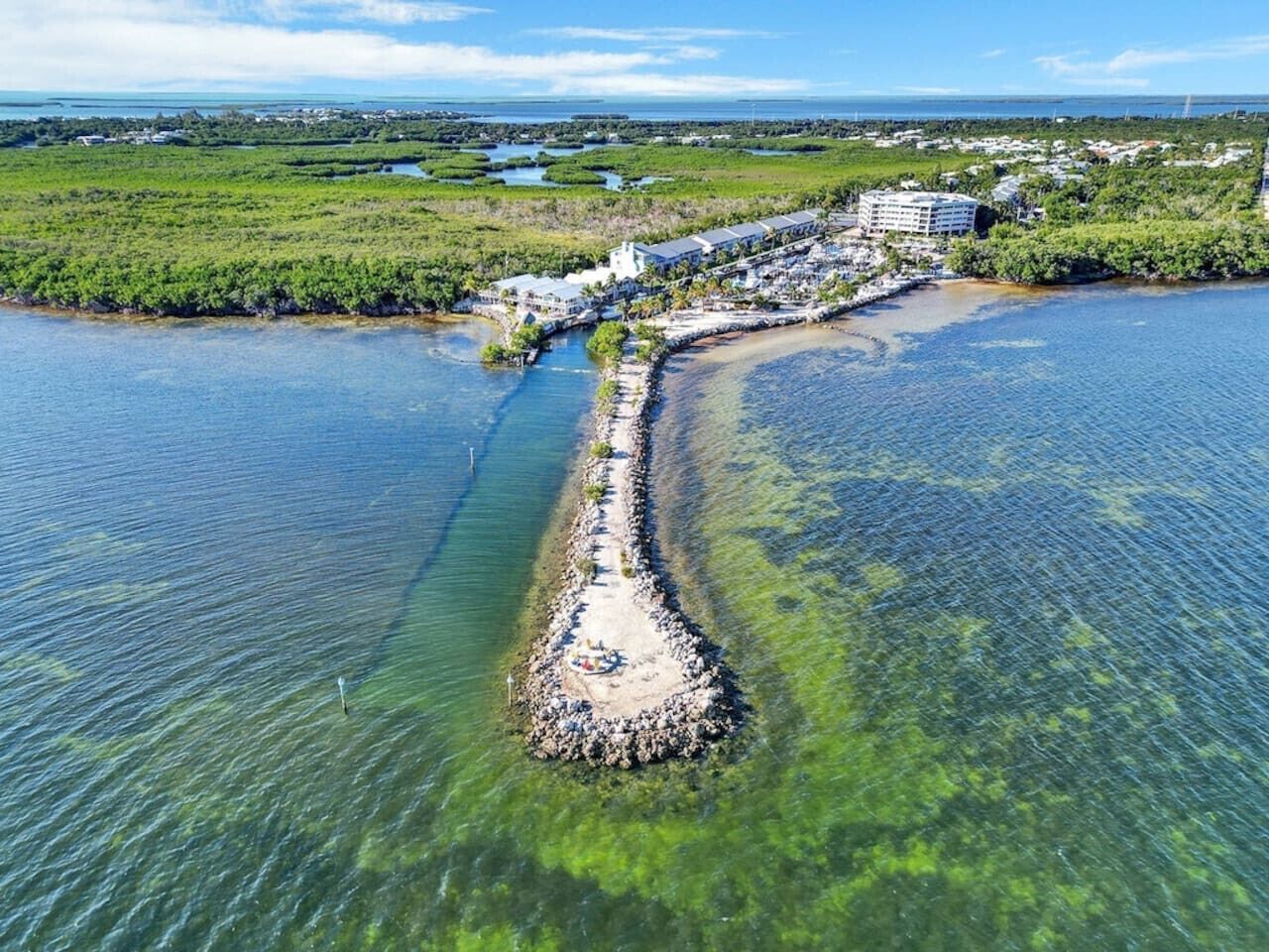 An aerial view of a coastal resort with a long, narrow peninsula extending into the water, surrounded by lush greenery and clear blue waters.